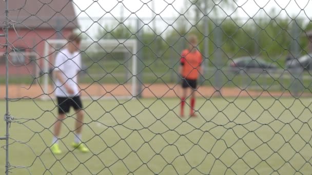 Молодые парни играют в футбол на стадионе за решеткой, на заднем плане, копируют пространство, замедленная съемка — стоковое видео