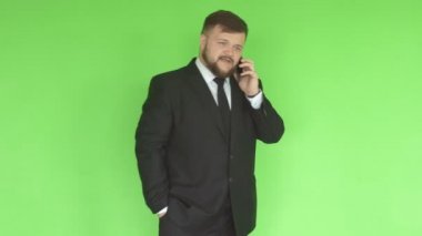 Sakallı siyah iş elbisesi giymiş beyaz bir adam, yeşil bir duvarın arka planında telefonla sorunları çözer,