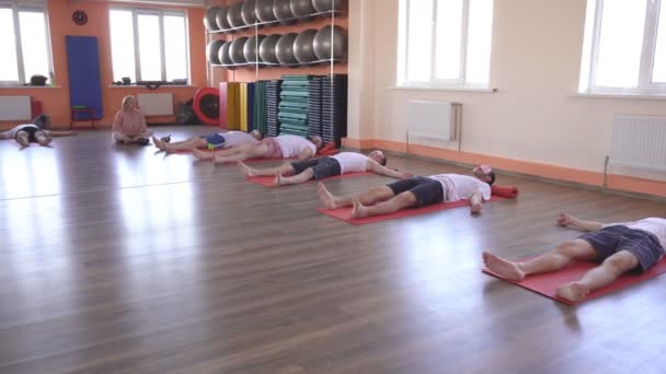 Mulher branca instrutora realiza aulas de ioga, postura shavasana, amigos do sexo masculino mentir e relaxar, restauração e renovação de todo o organismo, uma sensação de leveza e paz — Vídeo de Stock