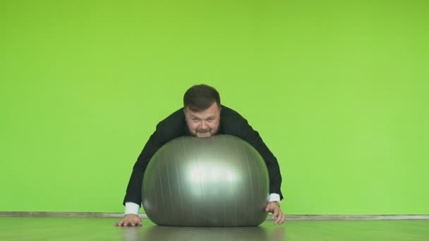 Funny plump man in black suit lies on exercise ball in fitness club or gym. Cheerful fat manager does physical jerks. Positive thick boss goes in for sports. Happy human emotions. Chromakey green. — Stock Video