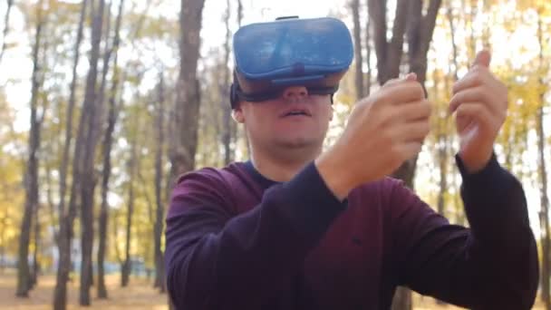 Gamer i virtual reality headset spiller et spil på solrig dag i efteråret park – Stock-video