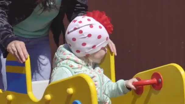 Little beautiful caucasian girl 3 years old plays with her mother in a modern playground for children, spring swing, happiness — Stock Video