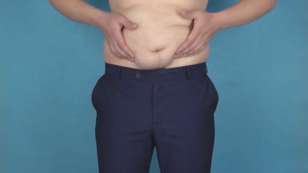 Ein junger Mann reibt seine Fettfalten auf einem dicken Anti-Cellulite-Magen, das Konzept eines falschen Lebensstils und einer falschen Ernährung, das Problem, Zeitlupe, Gesundheitswesen — Stockvideo