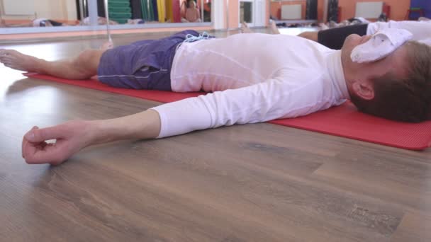 Mujer caucásica instructora conduce clases de yoga, postura shavasana, amigos masculinos mienten y se relajan, restauración y renovación de todo el organismo, una sensación de ligereza y paz, asana — Vídeo de stock