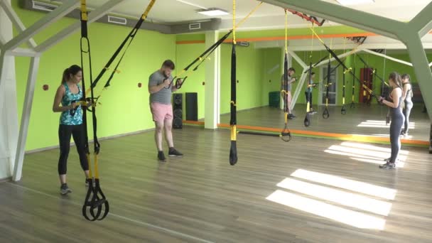 Människor i gymmet är engagerade på TRX loopar och utföra en förlängning övning på triceps, muskel förstärkning, övervikt, gymnasium — Stockvideo