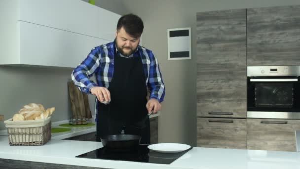 Um tipo gordo com uma barba num avental cortinas de milho para hambúrgueres. A carne frita-se em uma panela. Estilo de vida insalubre, comida rica em calorias. O risco de obesidade e sobrepeso. em câmara lenta . — Vídeo de Stock