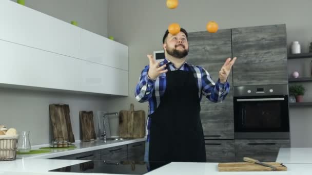 Momento engraçado alegre homem gordo joga laranjas para cima. Gordo a tentar fazer malabarismos e sorrisos, ri-se. A pessoa de Sobrepeso no avental felizmente olha. Slowmo vídeo . — Vídeo de Stock