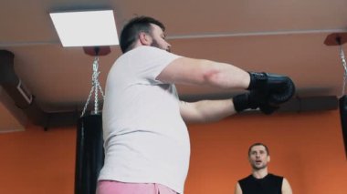 Boks eğitimi. Şişman adam ve ince kız eldiven birbirlerini selamlıyor. Kişisel koçum. Spor salonunda bireysel kilo kaybı matkaplar. Bir spor salonunda eğitmen ile egzersiz. Kalın adam için özel eğitmen. Yapı