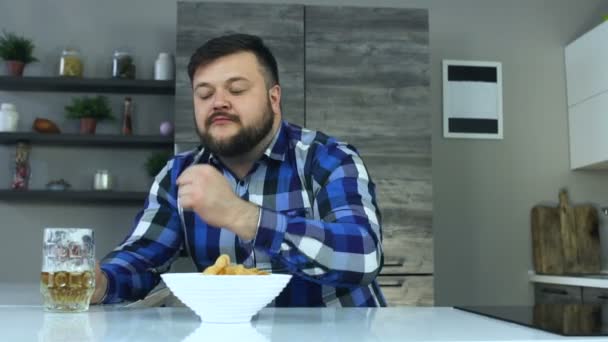 Thick guy with a beard eats crisps or potato chips and drinks beer in a mug. Unhealthy Lifestyle. Alcoholic drink and high calorie harmful food. The risk of obesity and overweight. — Stock Video