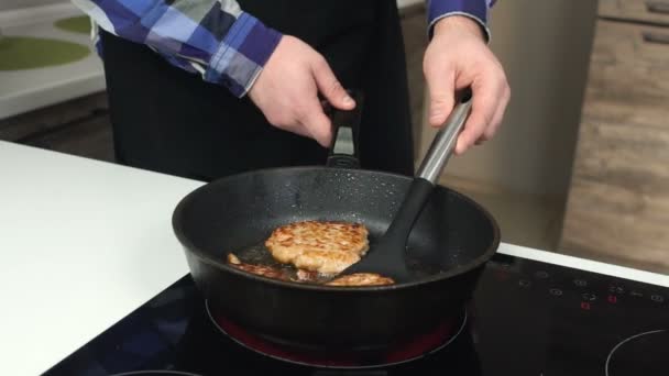 Pria gemuk dalam irisan apron kentang goreng pada kompor listrik menekan dan mengubahnya dengan spatula. Seorang pria tebal dalam apron memasak sayatan pada oven listrik menekan dan membalik mereka dengan spatula . — Stok Video