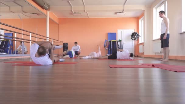 Класи йоги з індивідуальним інструктором з красивою кавказькою дівчиною в сучасному фітнес-центрі, чоловіки друзі роблять йогу, щоб зменшити зайву вагу і сприяти здоров'ю — стокове відео