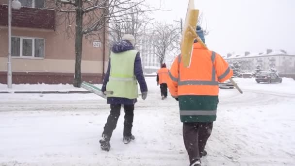 Eine Menschenmenge von Hausmeistern kommt mit Schneeschaufeln in die verschneite Stadt, Schneefall, Zeitlupe — Stockvideo