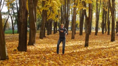 Sonbahar parkında dans eden komik ve eğlenceli kıvırcık adam. Güneşli bir günde bir kasabada yaprak düşer. Güzel doğa