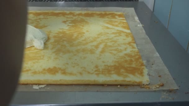 Confectioner sätter grädden på en kex rulle. Cake bageriprodukt. Manuell tillverkning av söt dessert med karamell eller smörkräm. Produktion av mjölkonfektyr. — Stockvideo