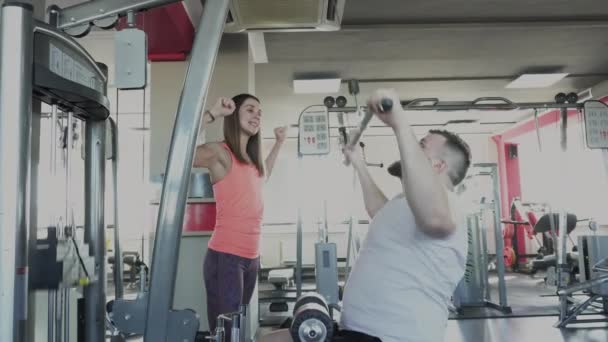 Hombre balancear los músculos de su brazo en simulador de entrenamiento en el gimnasio con instructor privado. Taladros de pérdida de peso de entrenador personal individual para el tipo gordo en el club de fitness. Persona gruesa haciendo ejercicios físicos — Vídeo de stock