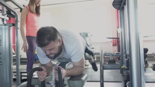 Guy Swing hans ben muskler på Training Simulator i gym med personlig instruktör. Viktminskning borrar från privata individuella tränare för fat man i Fitness Club. Tjock person som gör fysiska övningar — Stockvideo