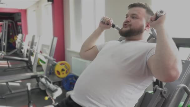 盖伊在健身房与私人教练一起在训练模拟器上摆动腿部肌肉。减肥训练从个人教练为胖子在健身俱乐部。做体育锻炼的胖人 — 图库视频影像