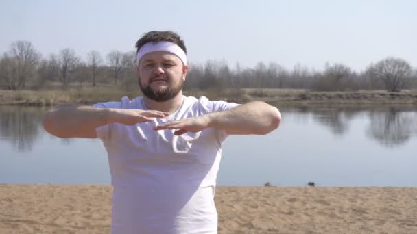 Vollbärtiger Mann im weißen T-Shirt beschäftigt sich mit Yoga-Technik über die Natur vor dem Hintergrund des Flusses, Kopierraum, meditative Technik — Stockvideo