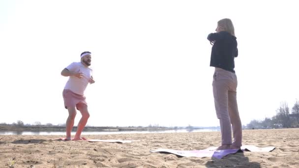 Um homem caucasiano e uma mulher praticam ioga dinâmica na margem do rio na natureza, técnicas meditativas, se livrar do estresse e braçadeiras musculares, auto-melhoria — Vídeo de Stock