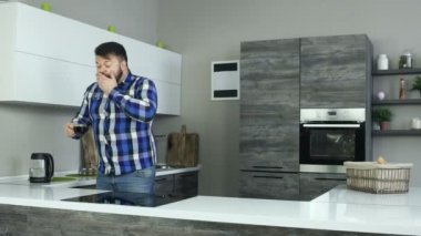 Uykulu bir adam mutfakta duruyor ve esneyor, kaşıkla kahve karıştırıyor. Uykulu bir adam mutfakta, esneme ve bir kaşıkla bir içki karıştırır.