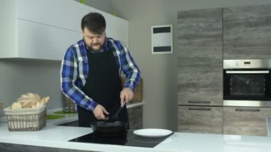 bir önlük şişman adam elektrikli fırın yakınında mutfakta duruyor ve bir spatula ile pirzola presler. Bir önlük kalın bir adam elektrikli ocak yanında duran mutfakta ve pirzola presler