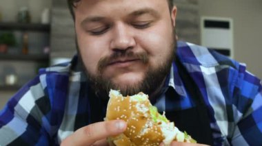 Sakallı şişman adam bir parça hamburger ısırır. Yemekler çok lezzetli. Tombul adam memnun. Sağlıksız Yaşam Tarzı, kızarmış ve yüksek kalorili gıda. Obezite ve aşırı kiloluluk riski. Yavaş çekim