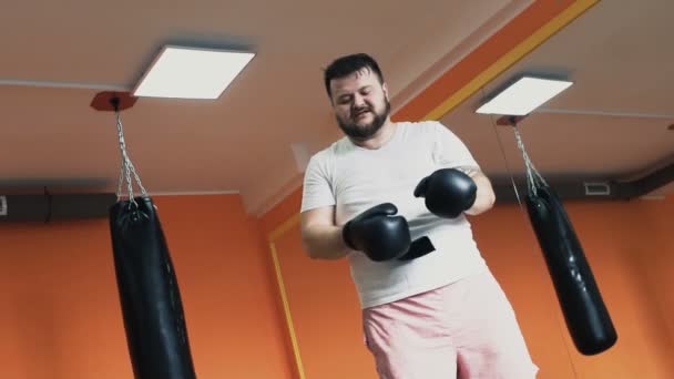 Толстый потный парень устал после тренировки и снимает боксерские перчатки в спортзале. Индивидуальные упражнения по снижению веса для толстого человека. Тренировка с инструктором в спортзале. Частный тренер для толстых мужчин — стоковое видео