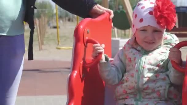 Pequena menina caucasiana bonita 3 anos de idade brinca com sua mãe em um parque infantil moderno para crianças, balanço de primavera — Vídeo de Stock