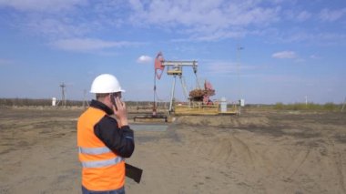 Bir pompa istasyonu petrol, gaz ve yanıcı yakıt endüstrisinin arka planda telefonda konuşan bir sinyal yelek erkek baş müfettişi, pumpjack, kopya alanı
