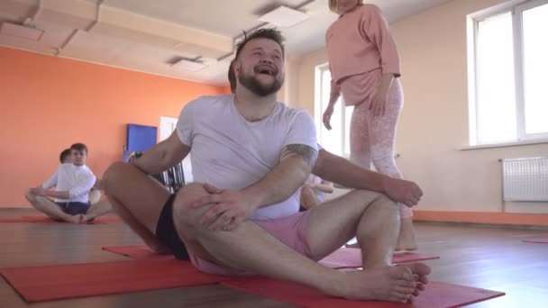 Yogalektioner med en individuell instruktör med en vacker kaukasisk flicka i ett modernt gym, manliga vänner som gör yoga för att minska övervikt och främja hälsa och hudton — Stockvideo