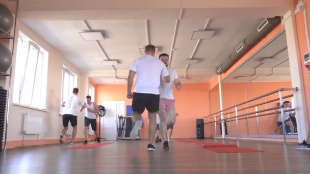 Hombres caucásicos guapos amigos entrenan en un gimnasio moderno en un entrenamiento de vapor de grupo para desarrollar resistencia y quemar el exceso de peso, ropa deportiva — Vídeo de stock