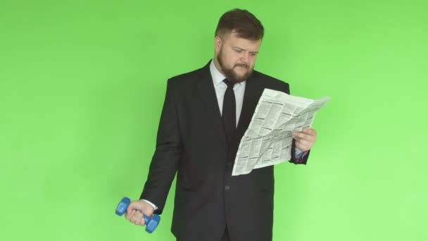 Knappe jonge Kaukasische mannelijke manager zakenman in zwart pak is bezig met een sportschool met dumbbells en leest Nieuws uit de krant, concept van gebrek aan tijd om te spelen sport, groene achtergrond — Stockvideo