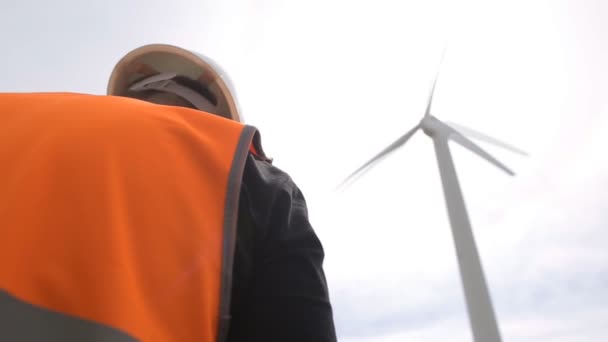 Um engenheiro masculino realiza uma inspeção e inspeção de uma turbina eólica que gera eletricidade girando as lâminas com o vento, um gerador de vento e a indústria, energia elétrica — Vídeo de Stock