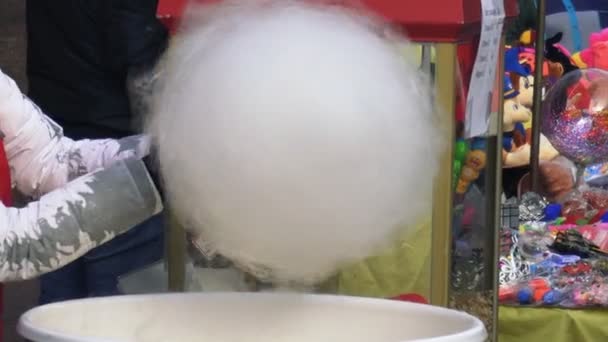 Una persona hace girar grandes dulces de algodón blanco con una máquina automatizada en una feria de diversiones. Un vendedor hace hilo de azúcar blanco con una máquina moderna en el parque de atracciones . — Vídeos de Stock