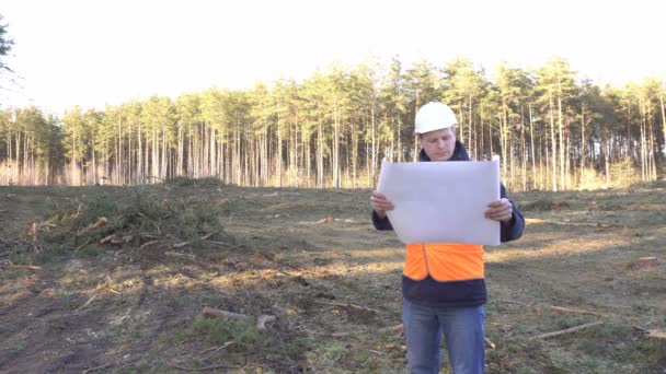 Un constructor masculino caucásico mira un plan de construcción y deforestación para un sitio para la construcción de un nuevo edificio, un arquitecto — Vídeos de Stock