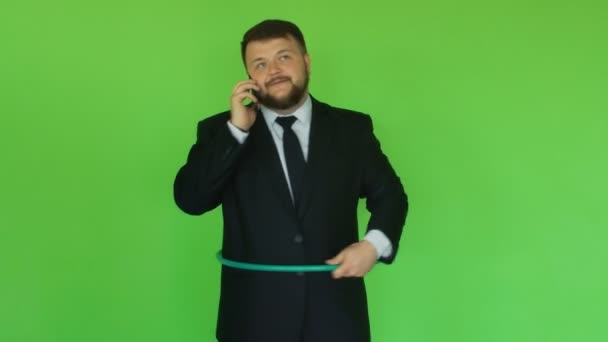 Hombre barbudo alegre y positivo en traje con aro hula hablando por teléfono. Una situación graciosa. Chromakey Green. Chico grueso barbudo en chaqueta negra, camisa y corbata resuelve problemas por teléfono inteligente. Hombre. — Vídeo de stock