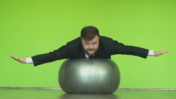 L'homme en costume repose sur un ballon d'exercice avec les mains comme des ailes vole comme un avion ou un oiseau dans un club de fitness. Enthousiaste gestionnaire de graisse fait des secousses physiques dans la salle de gym. Patron épais positif va dans le sport. Heureux — Video