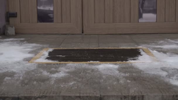 Человек отстряхивает ноги от снега перед входом в здание, крупным планом, зимой — стоковое видео