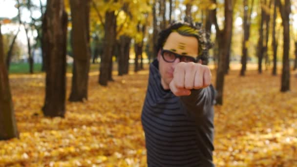 スーパーヒーローのような男は拳で手を伸ばし、秋の公園でカメラに飛びます。晴れた日に町に葉が落ちる。美しい自然 — ストック動画