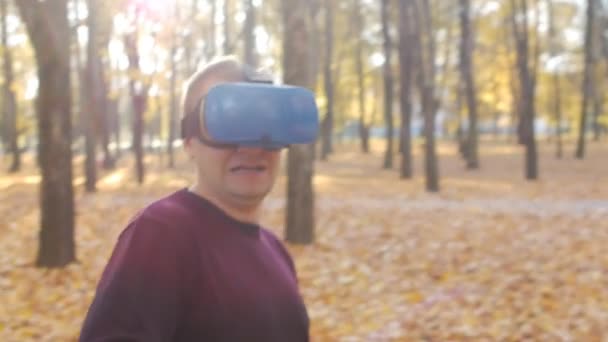 Cara no fone de ouvido realidade virtual está jogando um jogo no dia ensolarado no parque de outono — Vídeo de Stock