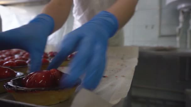 Αρτοσκευάσματα με γέμιση. Ο εργαζόμενος διπλώνει τούρτες σε συσκευασίες. Κέικ σε μορφή καλαθιού με φρούτα και μούρα, προϊόντα αρτοποιίας. Παρασκευή γλυκών γλυκών με φράουλα. Παραγωγή αλεύρων. — Αρχείο Βίντεο