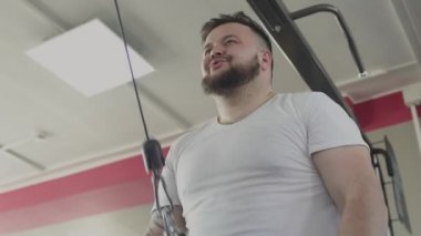 Şişman adam spor salonunda eğitim simülatörü onun kol kasları swing. Fiziksel gerizekalı yaparken kilolu adam kalori yakmak. Tombul erkek spor kulübünde Fitness egzersizleri yapıyor. Kalın obez erkek ve sağlık
