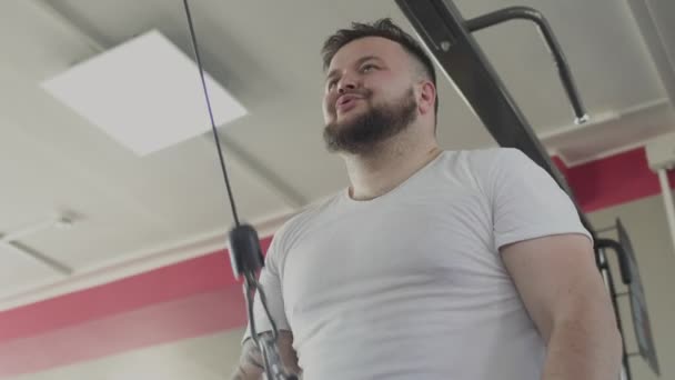 Fat Man Swing zijn arm spieren op training simulator in de sportschool. Overgewicht kerel verbranden calorieën terwijl het doen van fysieke schokken. Mollige man doet fitnessoefeningen in Sport Club. Dikke zwaarlijvige man en gezondheid — Stockvideo
