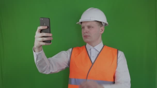 Constructor o ingeniero toma fotos en el teléfono inteligente de las obras de construcción. Chromakey. Jefe o jefe en un casco blanco y chaleco naranja toma una foto del proceso de construcción. Mercado inmobiliario . — Vídeos de Stock