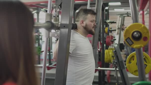 체육관에서 큰 복부를 가진 남자에 대한 여자 강사와 개인 훈련. 개인 코치와 함께 두꺼운 뚱뚱한 사람은 피트니스 센터에서 물리적 바보와 운동을합니다. 과체중 인 사람은 칼로리를 태웁니다. — 비디오