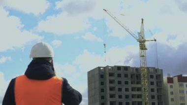 İnşaatçı, inşaat işlerinden telefonda konuşuyor. Binaya odaklan. Mühendis veya Boss beyaz bir kask ve turuncu yansıtıcı yelek veya yelek azarlar veya astları azarlar. İş Şefi