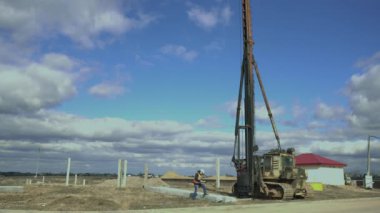 Mühendis çekiç ile eski bir izlenen Sovyet Kazık sürücüsünün yanındaki panoya veri yazar. Emlak piyasası. Konut inşaatı. Oluşturucu not defterindeki bilgileri denetler. Patron