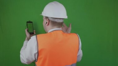 İnşaat işleri hakkında Selfie modu ile görüntülü Konferans araması yapan mühendis veya oluşturucu. Kromatkey. Patron veya kulaklık şefi, beyaz kask ve turuncu yelek raporları müşteriye