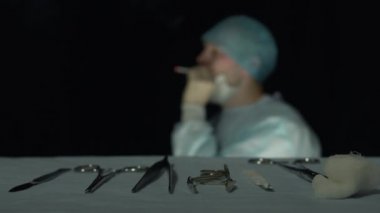 Yorgun cerrah hastanede ameliyat veya işlemden sonra sigara içer. Neşter, kavrayıcı, forcep, cılız gibi cerrahi aletlere odaklanın ön planda