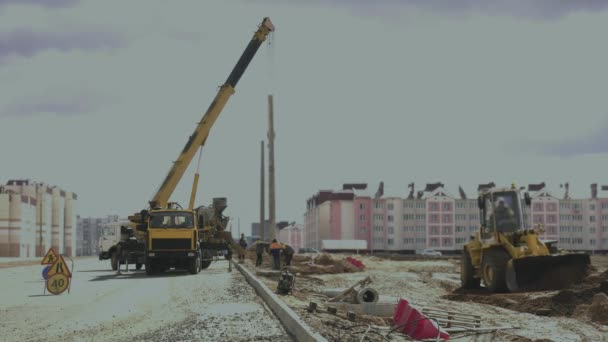 Workers install a pole with street light by automobile crane along the road. Construction machinery, concrete or cement mixer transport truck are on the work zone. Engineers set up lamppost on highway — Stock Video